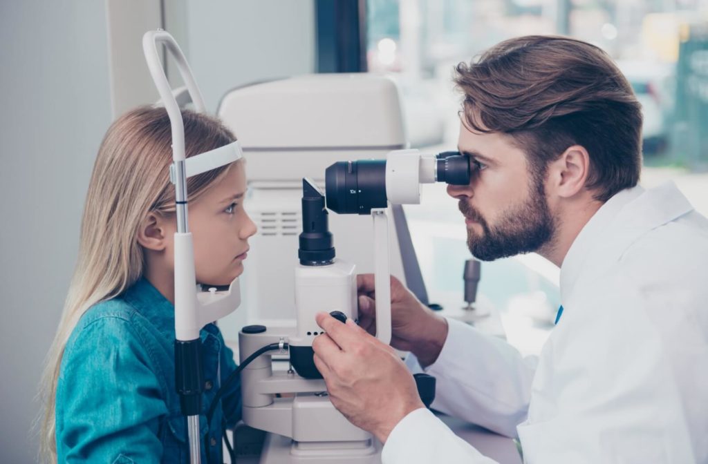 A male optometrist examining the eyes of a young child using a medical device to detect potential eye problems.