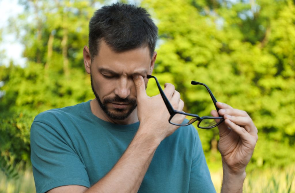 Man rubbing his eyes while holding glasses, experiencing discomfort from dry eyes.