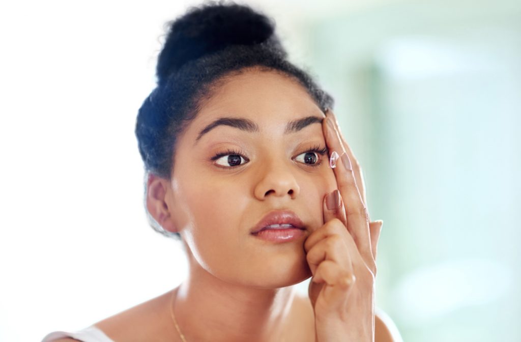 A young woman is focused while she applies her contact lens to her right eye.