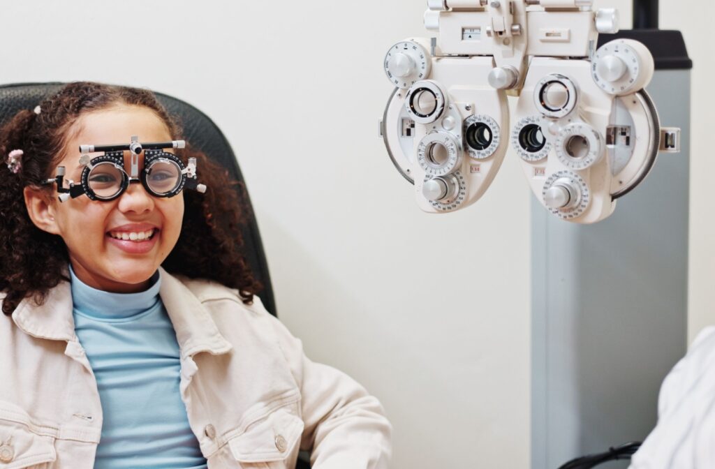 Smiling child wears a phoropter trial frame during an eye exam at an optometry clinic