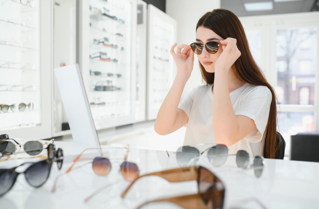 A person tries on sunglasses in an eyewear store, surrounded by display racks.