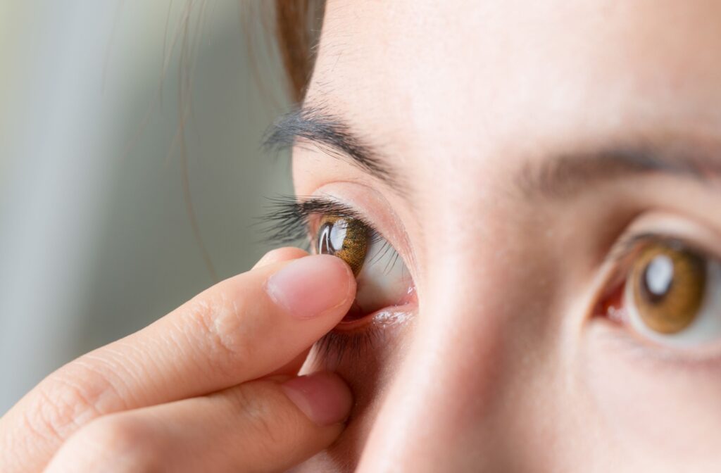 An adult gently pinches their contact lens with their thumb and index finger to remove it.