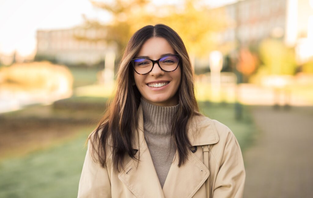 A young adult smiles while wearing a brand new pair of eyeglasses, leading to relief from blurry vision and headaches.