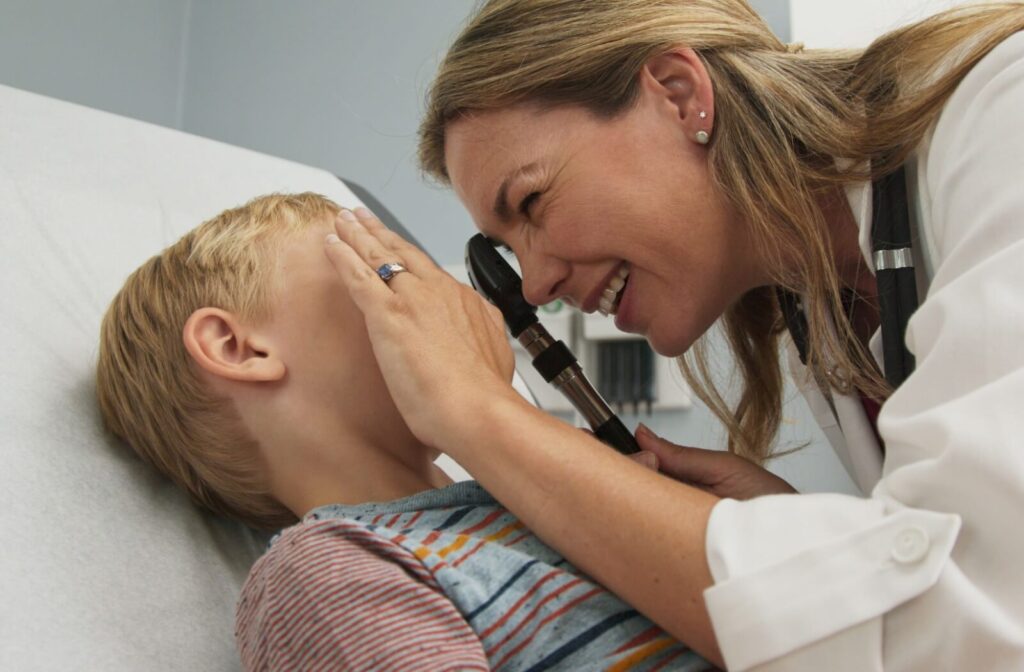 An optometrist performing a vision test on a young boy using an ophthalmoscope to examine his eyes during a pediatric eye exam.