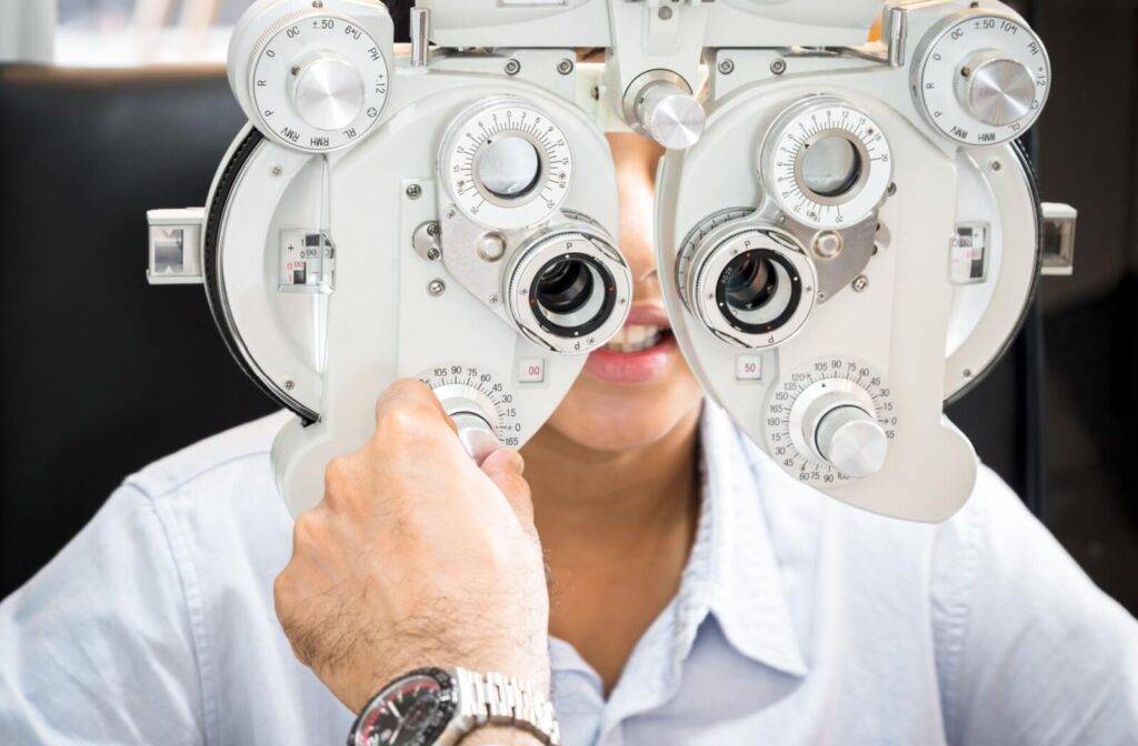 Optometrist performing a vision test using a phoropter to determine a patient’s eyeglass prescription during an eye exam.