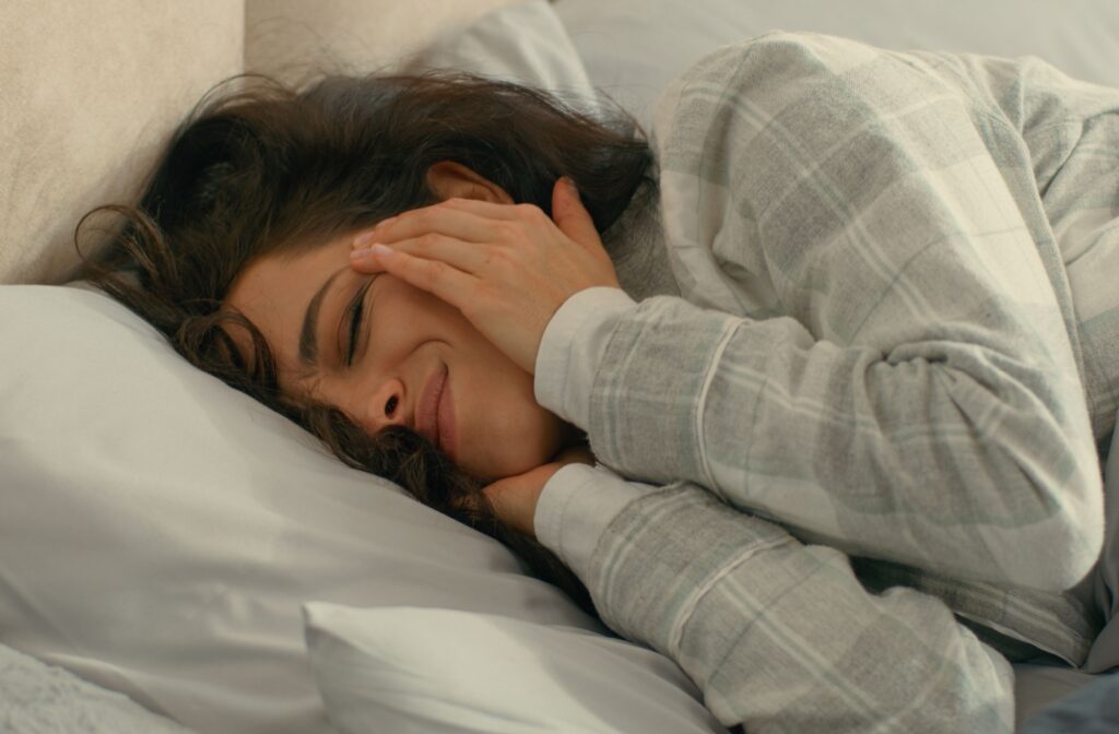 A person holding their temples and squinting as they experience eye pain upon waking up in the morning